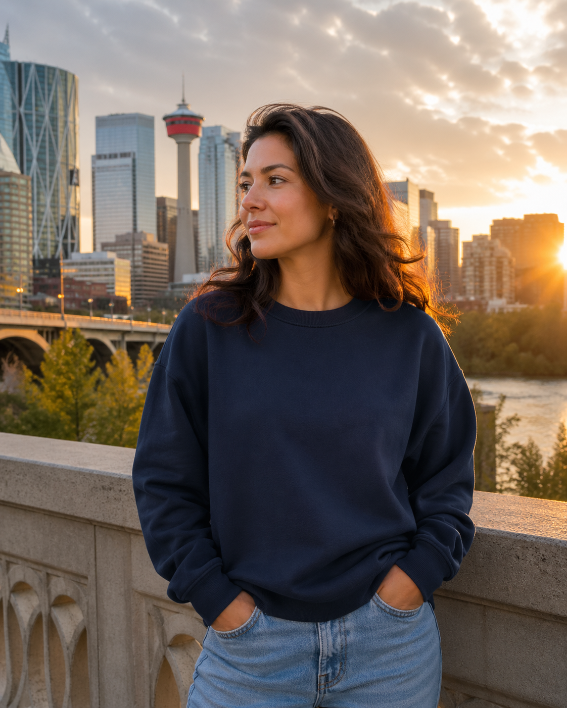 Woman wearing a navy crewneck sweatshirt with the Calgary skyline at sunset